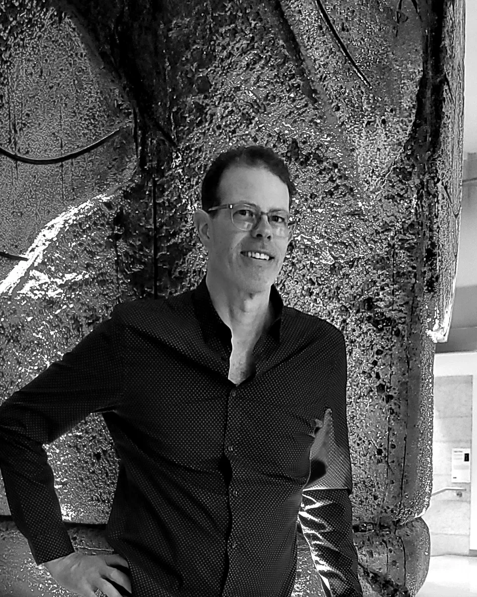 Louis Tremblay, debout, en chemise, devant une sculpture de pierre